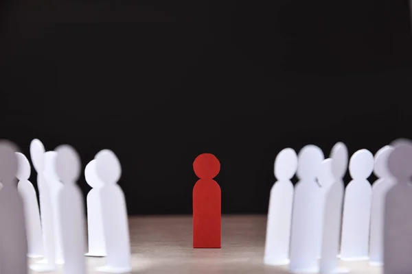 social discrimination concept with many little white paper men around a different one on wooden base and dark background front view