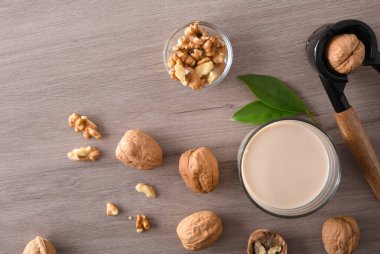 Bir bardak dolusu ceviz ve meyve dolu sebze sütü ve fındık kıracağıyla ahşap masa. Üst görünüm.