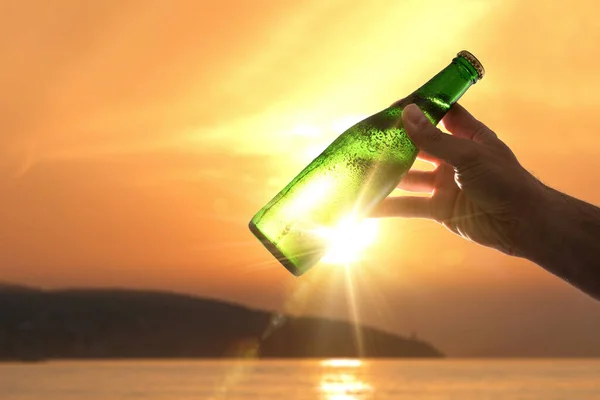 Hand Raising Bottle Fresh Beer Backlit Sunset Sun Shoreline Background — Stock Photo, Image