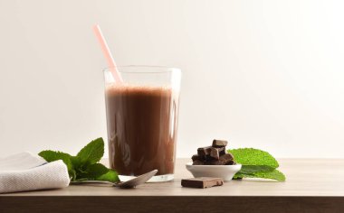 Bardakta çikolatalı milkshake, çikolata porsiyonlu, ahşap bankta ve izole bir arka planda. Ön görünüm.