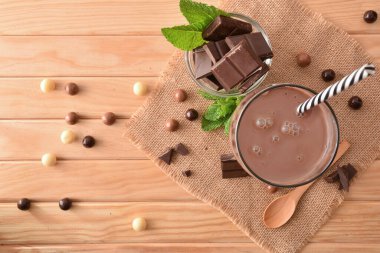 Çikolatalı bardak, ahşap masada sallanıyor. Çikolata ve nane yaprakları üst tarafta.