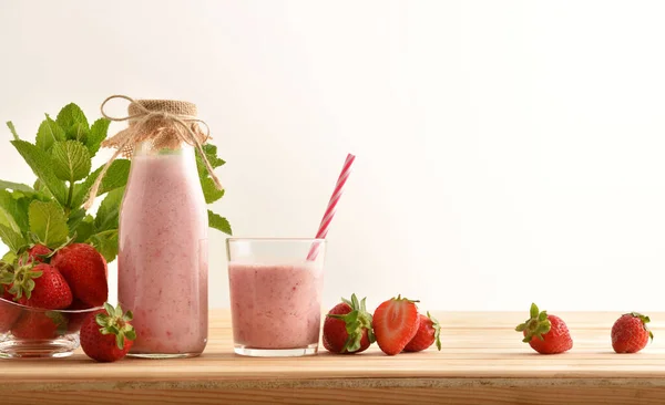 bottle and glass full of strawberry smoothie on wooden table full of fruits isolated background. Front view.