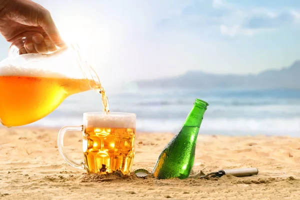 用一个男人的手从杯子里倒入一杯啤酒来冷却海滩的想法 前景细节 — 图库照片