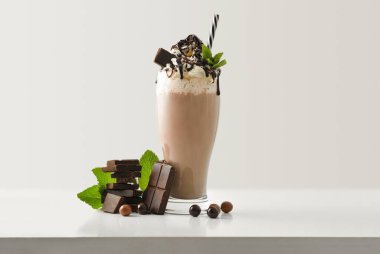 Çikolatalı milkshake, kremalı çikolata porsiyonları ve beyaz ahşap masanın etrafında toplar ve ışık yalıtılmış arka plan. Ön görünüm.