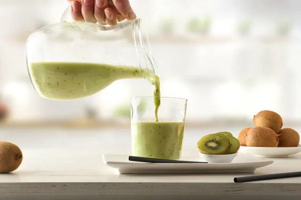 Person serving kiwi drink from jug with cut fruit in containers on kitchen bench. Front view.