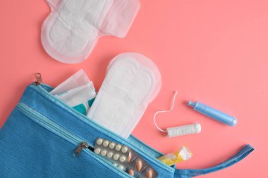 İçinde çeşitli regl hijyen ürünleri ve pembe arka plandaki kadınlar için haplar olan tuvalet çantası. Üst görünüm.