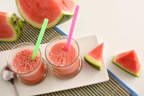 Two glasses with natural watermelon juice on a plate on white kitchen bench with cut fruit. Top view.