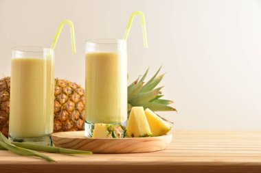Sütlü ananas suyu ve ahşap masa üzerinde beyaz izole edilmiş ananas porsiyonlu iki uzun bardak..