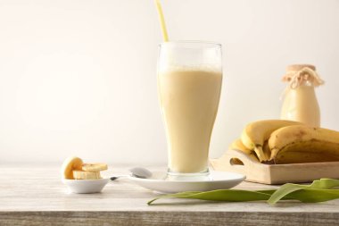 Muzlu milkshake, cam bardakta muz, tepside meyve ve beyaz yalıtılmış arka plan. Ön görünüm.