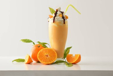 Kremalı turuncu milkshake, meyve ve yapraklarla süslenmiş beyaz masa ve ışık yalıtılmış arka plan. Ön görünüm.