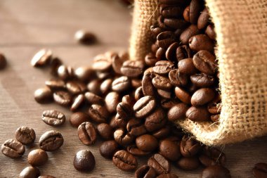 Çuval dolusu kahve çekirdeğini ahşap masaya yakın tut. Manzara yükseldi. Yatay bileşim.