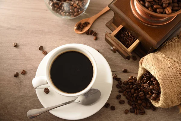 Cup of coffee with sack full of beans and manual grinder on wooden table. Top view. Horizontal composition.