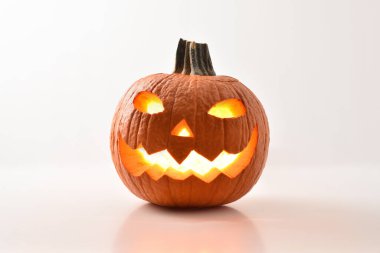 Cadılar bayramı için hazırlanmış oyulmuş ve aydınlatılmış balkabakları beyaz masaya ve izole edilmiş beyaz arka plana yansıyor. Ön manzara. Yatay bileşim.