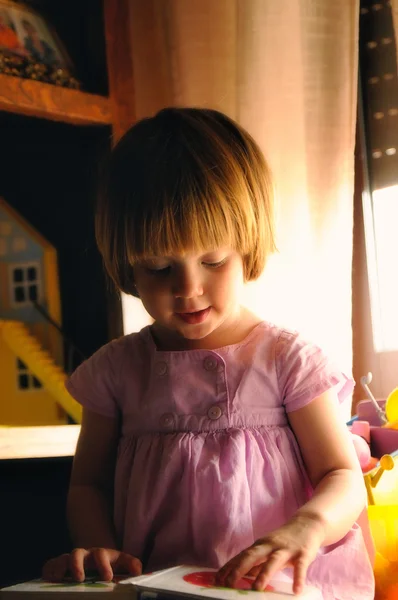 Niña viendo un libro educativo sobre una mesa en una habitación —  Fotos de Stock