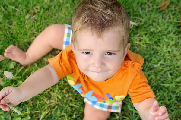 Blond dziecko siedzi na trawie z gałązka w ręku — Zdjęcie stockowe