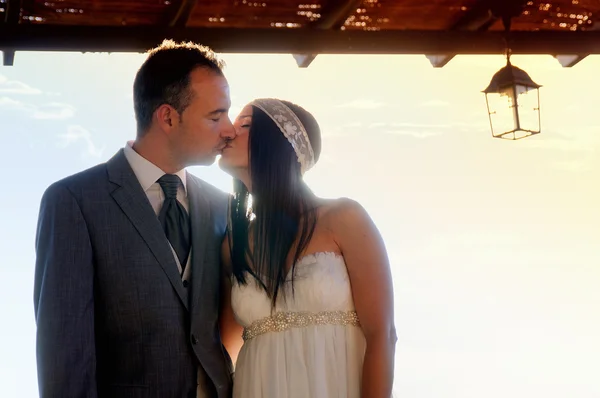 Bride and groom kissing under a porch at sunset — Stock Photo, Image