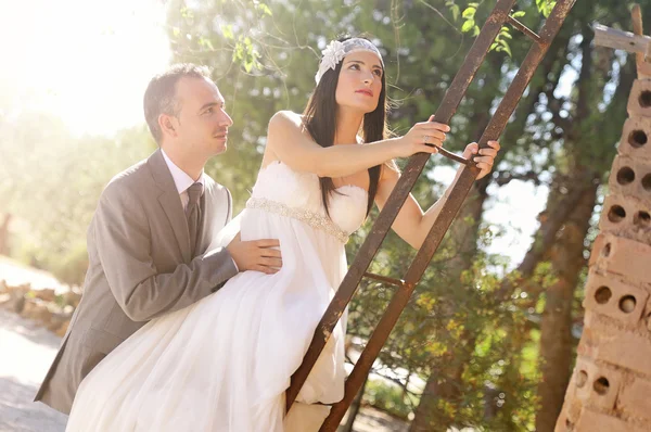 Groom and bride climbing a rusty ladder — Stock Photo, Image