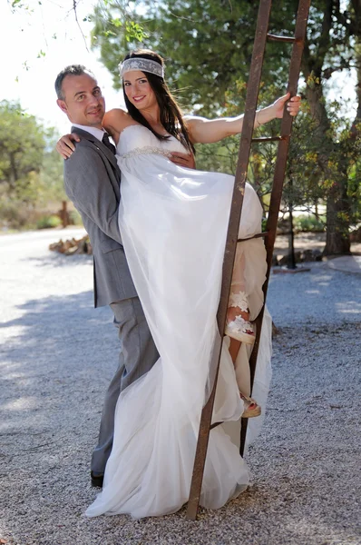 Groom and bride fun climbing a rusty ladder — Stock Photo, Image