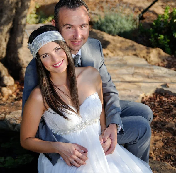 Groom holding the bride sitting on a rock outdoor — Stock Photo, Image