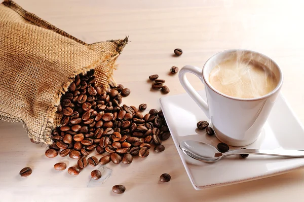 Ζεστό φλιτζάνι καφέ πίνακα και σάκο με κόκκους καφέ — Φωτογραφία Αρχείου