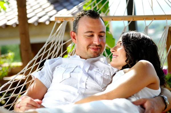 Young couple on a rope hammock in a cottage front view — Stock Photo, Image