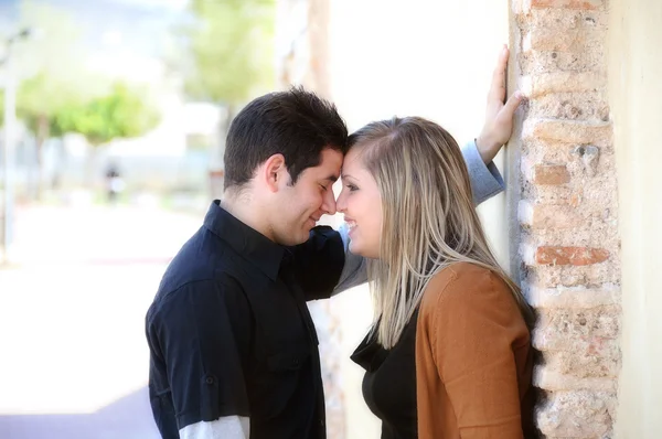 Young couple flirting against a brick wall in a park — Stock Photo, Image