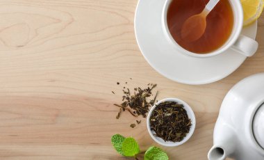 Beyaz seramik bir fincanda limonlu siyah çay ve bir tas kuru çay yapraklarıyla dolu ahşap bir masada çaydanlık içeren arka plan. Üst görünüm.