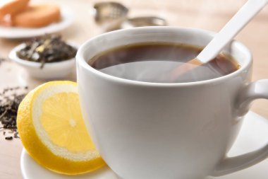 Beyaz seramik bir fincanda limonlu siyah çay, ahşap bir masada malzemeler ve hamur işleriyle birlikte. Yüksek görünüm.