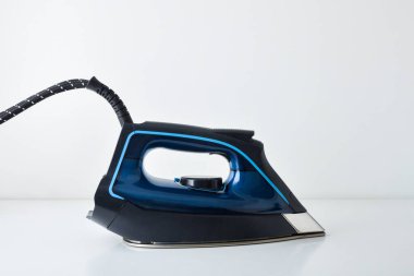 Yansıma ve beyaz izole arkaplan ile beyaz masa üzerinde dinlenen buhar demiri. Ön görünüm.