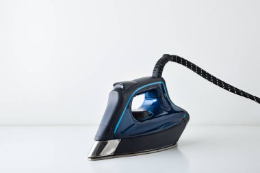 Mavi buharlı ütünün ön tarafı beyaz masaya ve beyaz izole arka plana yansıyor. Ön görünüm.