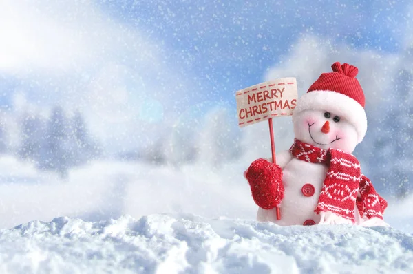 Muñeco de nieve con un cartel Feliz Navidad en la nieve — Foto de Stock