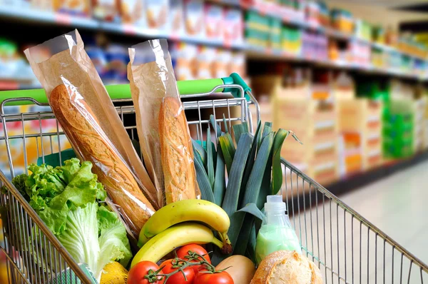 Shopping cart full of food in supermarket aisle elevated view — Stock Photo, Image