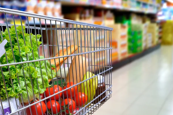Carro de compras lleno de comida en el pasillo del supermercado inclinación lateral — Foto de Stock