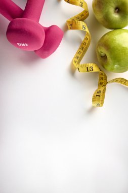 Pink dumbbells with apple and tape measure vertical composition 