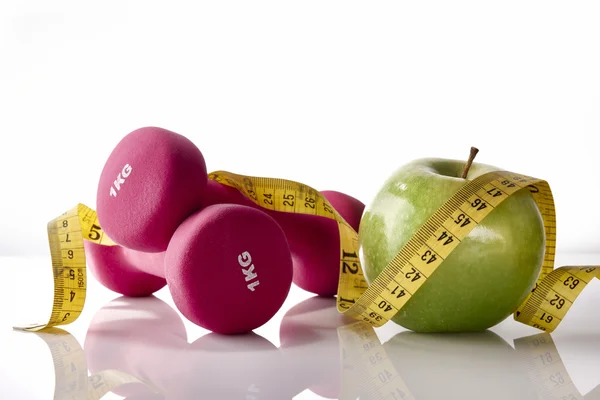 Apple dumbbells and tape measure on white glass table front — Stok fotoğraf