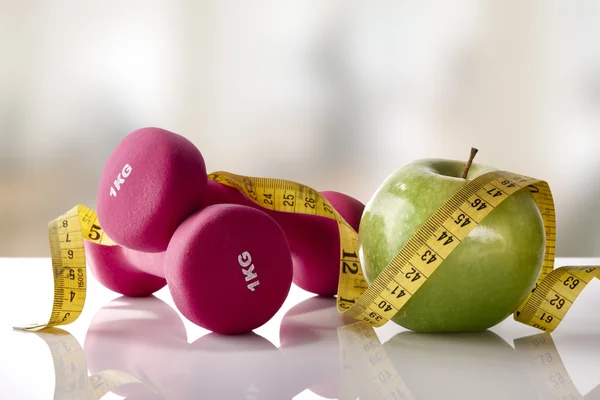 Mancuernas de manzana y cinta adhesiva en frente de gimnasio de mesa de vidrio blanco —  Fotos de Stock