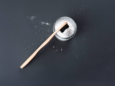 Gri arka planda bardakta diş pudrası olan bambu bir diş fırçası..