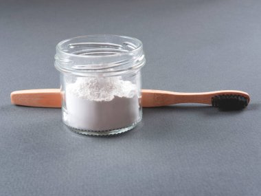Gri arka planda bardakta diş pudrası olan bambu bir diş fırçası..