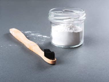 Gri arka planda bardakta diş pudrası olan bambu bir diş fırçası..
