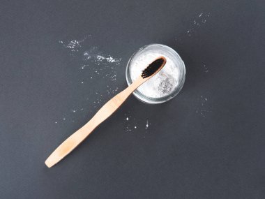 Gri arka planda bardakta diş pudrası olan bambu bir diş fırçası..