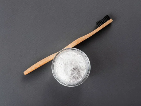 Brosse à dents en bambou avec poudre à dents dans un verre sur fond gris. — Photo