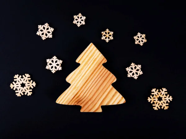 The zero waste new year concept as a wooden conifer tree and falling wooden snowflakes on the black background. — Stock Photo, Image