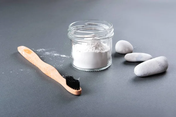 Concepto de cero residuos para la limpieza de dientes. El cepillo de dientes de bambú con el polvo de dientes en el vidrio y tres piedras sobre el fondo gris. — Foto de Stock