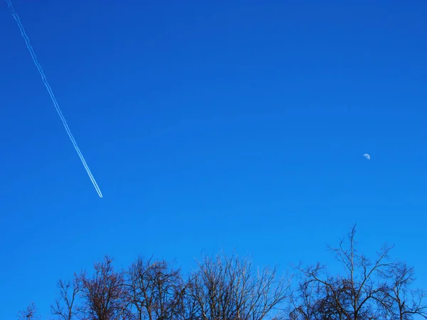 The beautiful blue sky with a plane and the moon on it on a sunny day. Winter or spring natural background. Selective focus.