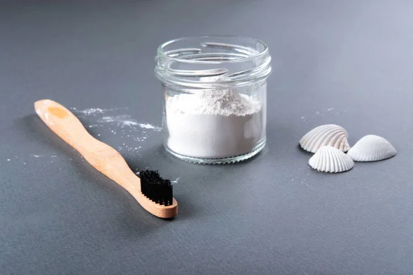 Concept zéro déchet pour le nettoyage des dents. La brosse à dents en bambou avec la poudre à dents dans le verre et trois coquilles blanches sur le fond gris. — Photo