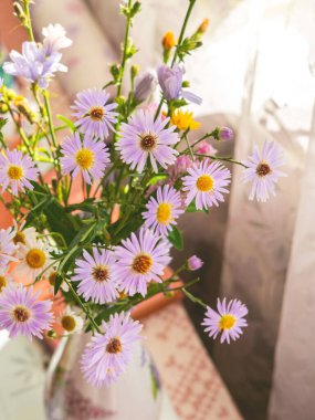 Pencerenin yanındaki masada soluk mor astar demetleri..