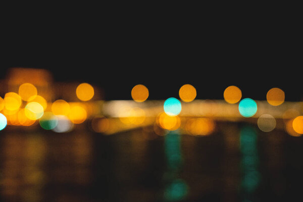 The beautiful blurred background of the city bridge across the river at night with the bokeh lights and festive reflections in the water.