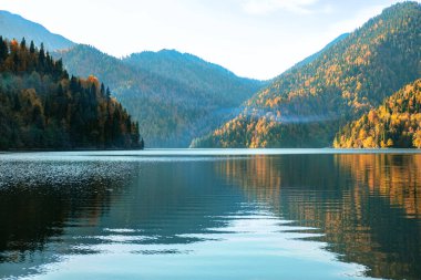 Dağdaki Ritsa Gölü 'nün güzel manzarası tepelerdeki renkli sonbahar ağaçları ve sudaki yansıması, sonbahar manzarası..