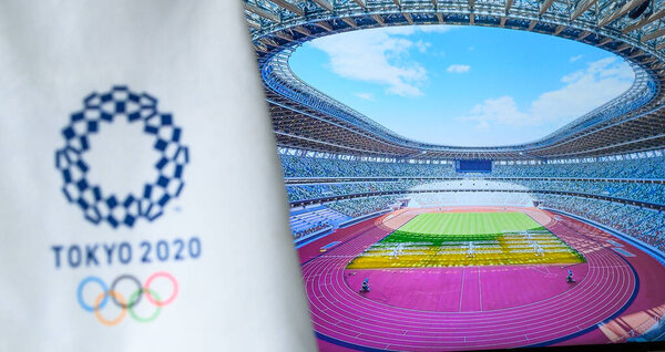 TOKYO, JAPAN, JULY. 19. 2021: Olympic Stadium in Tokyo, Summer olympic Game logo on white background in foreground. Athletics track, Stadium in daily light.