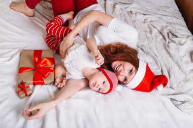 Noel Baba şapkalı anne ve bebek yatakta oturuyor ve evde kalıyorlar. Xmas ve Yeni Yıl